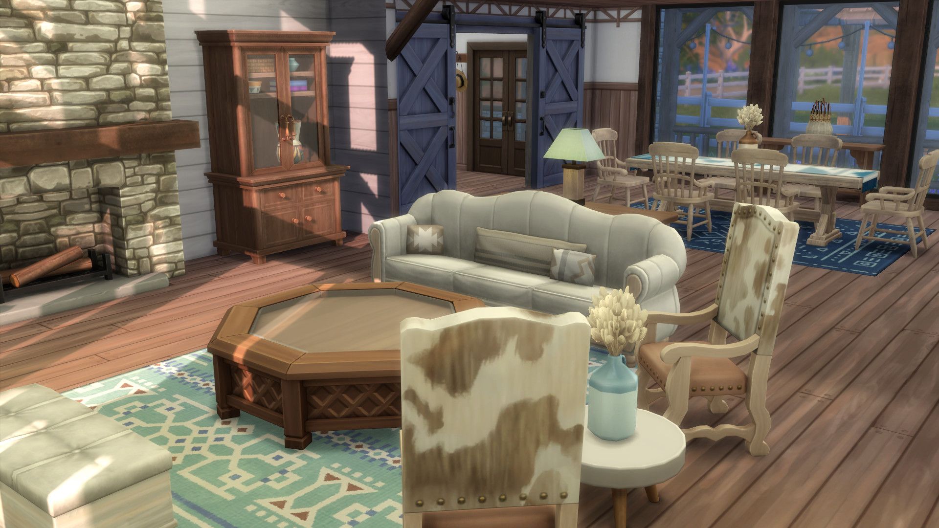 Intérieur de la maison Sims 4 vie au ranch montrant une cheminée, une table à manger et une table basse avec des chaises à imprimé vache.